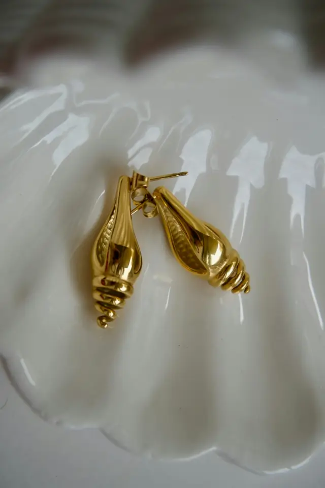 Des boucles d'oreilles dorées en forme de coquillage dans une coupelle blanche
